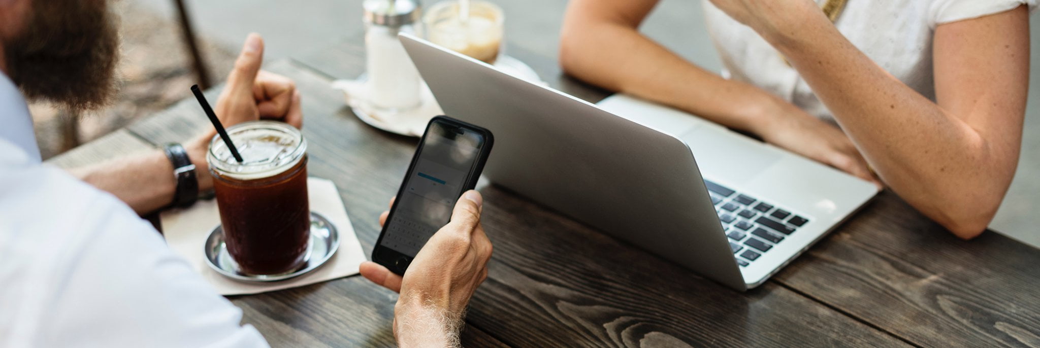 Duas pessoas em uma reunião numa cafeteria, com smartphones e notebook