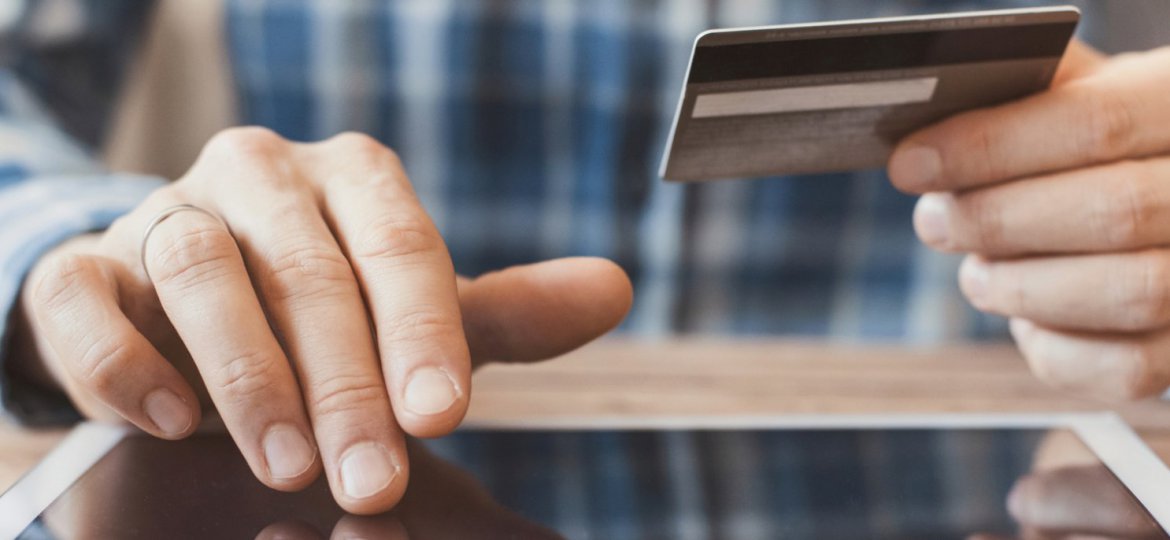 Homem fazendo uma compra online em seu tablet, segurando o cartão de crédito