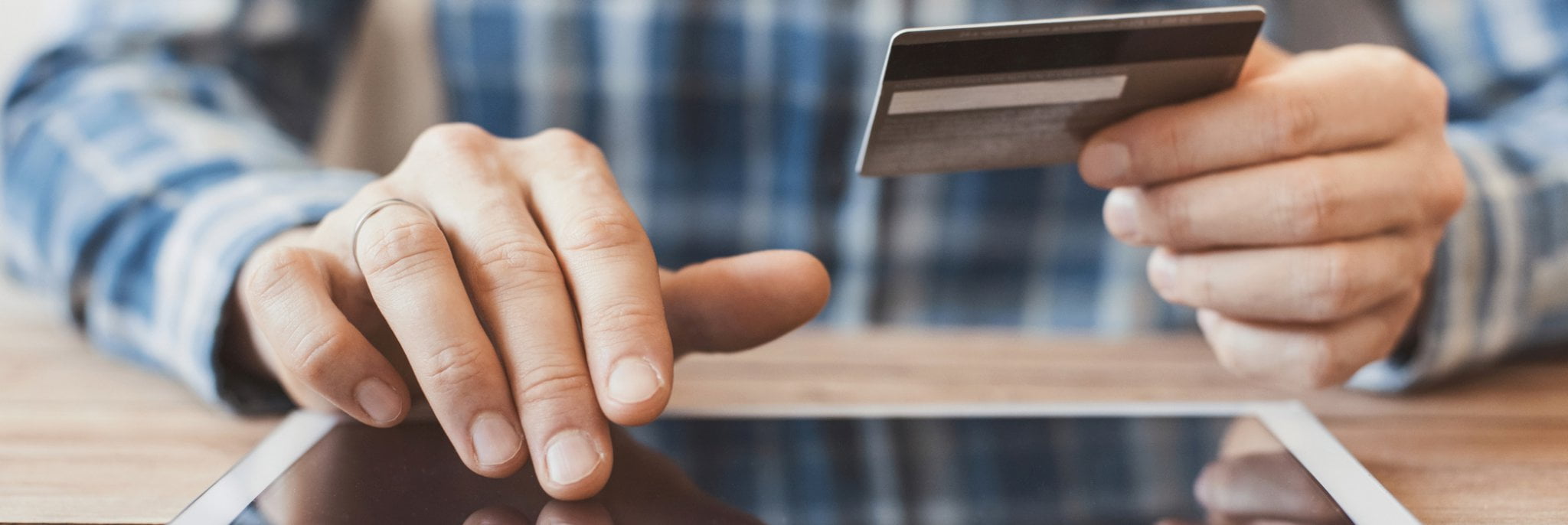 Homem fazendo uma compra online em seu tablet, segurando o cartão de crédito